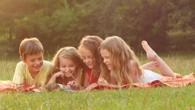 Boy and girls read a book in the garden lying on the blanket beautiful summer day. Close up