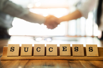 success word on wood table with business man shaking hands during a meeting in the office, dealing, greeting and partner concept background
