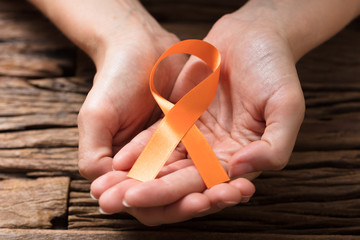 Human Hand Showing Orange Ribbon To Support Breast Cancer Cause
