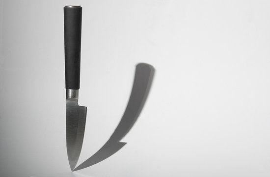 Knife with black handle and it shadow on white background. Food concept. Copy space for text.