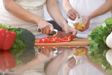 Close-up of four human hands are cooking in a kitchen. Friends having fun while preparing fresh salad. Vegetarian, healthy meal and friendship concept