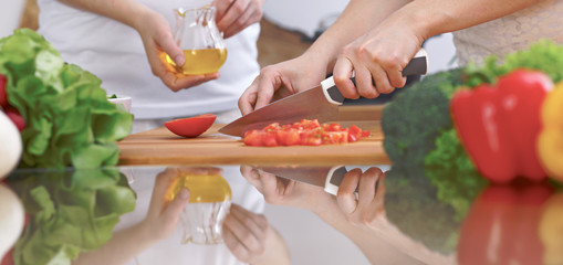 Close-up of four human hands are cooking in a kitchen. Friends having fun while preparing fresh salad. Vegetarian, healthy meal and friendship concept