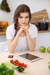 Young brunette woman is cooking and tasting fresh salad in the kitchen. Housewife holding wooden spoon in her hand