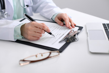 Close-up of a female doctor filling  out application form , sitting at the table in the hospital