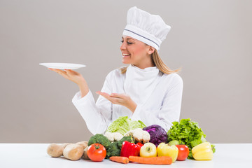 Portrait of cheerful female chef sitting at the table and showing empty plate while making healthy meal.