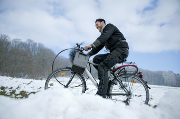 Schornsteinfeger fährt mit Fahrrad und Arbeitsgerät durch verschneite Winter Landschaft