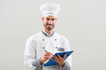 Smiling chef is holding cookbook and writing a new recipe.