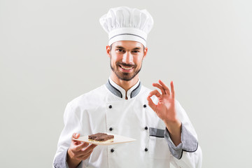 Confectioner is showing slices of cake and ok sign on gray background.