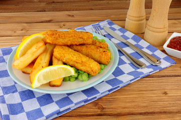 Batter covered fish fingers and chips meal with mushy peas on a wooden background