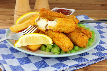 Batter covered fish fingers and chips meal with mushy peas on a wooden background