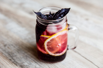 Black-currant lemonade with lemon slices, berries, ice cubes and purple basil in a glass jar. Selective focus.
