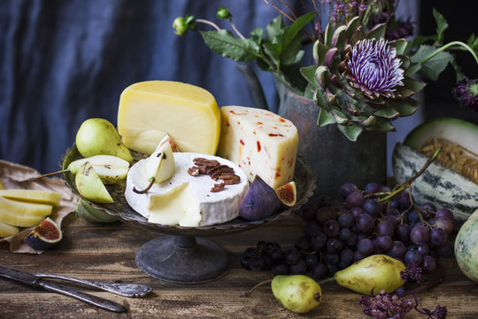 The different cheese, fresh fruit and garden flowers on old wooden table and blue background