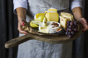 Young woman holding a plate of cheese on the wooden board