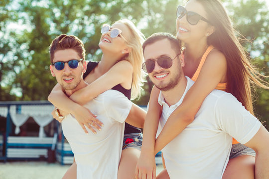 Group of friends walking along the beach, with men giving piggyback ride to girlfriends.
