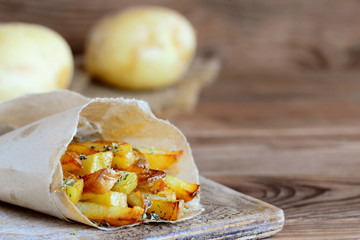 Crispy fried potatoes with spices. Country fried potatoes in paper and on a wooden table. Rustic...