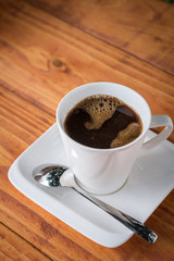 White cup of coffee with metal spoon on the plate