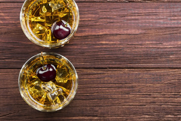 Cocktail from whisky with cherry in two glasses on a wooden background. Top view, copy space. Food background