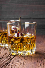 Cocktail from whisky with cherry in two glasses on a wooden background