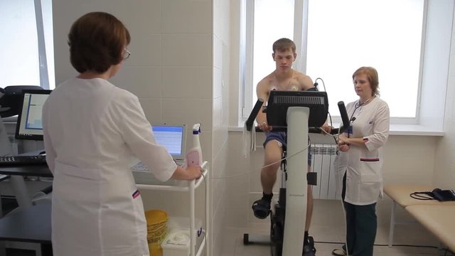 Two women of a medical doctor perfrorms an electrocardiographic study using an exercise bike and computer technology