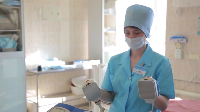 A female surgeon prepares a defibrillator for a surgical operation. New medical technologies