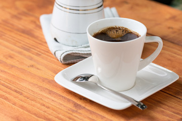 Cup of coffee with metal spoon on the plate on the wooden board table