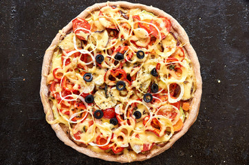 Hot vegetarian pizza with tomatoes, bell pepper, onion, black olives, cheese, spices on black dark background close up. Top view