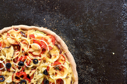 Hot vegetarian pizza with tomatoes, bell pepper, onion, black olives, cheese, spices on black baking tray dark background close up with copy space. Top view