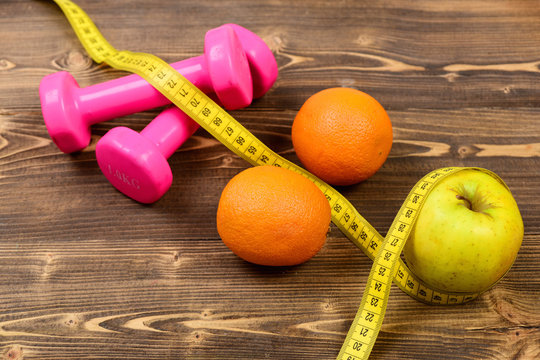 sport concept, dumbbells weight with measuring tape, orange and apple