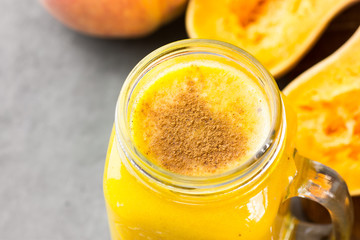 Glass mason jar with raw pumpkin butternut squash smoothie with peaches, bananas, spices. Ingredients on dark stone table. Bight colors, top view.