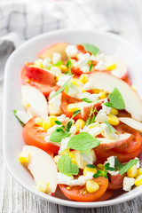 Summer salad with tomatoes, peaches, corn, feta, mint and honey vinaigrette. Selective focus, close up.