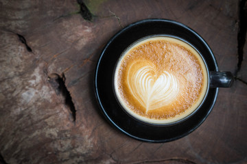 Cup of latte art coffee with heart shape on wooden texture