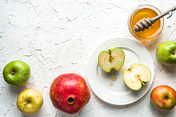 Halves of apples on a plate, pomegranate and honey on a white table