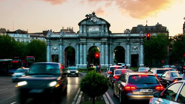 Night view of The Puerta de Alcala at sunset in Madrid, Spain - a monument in the Independence Square. Motion blurred cars and buses, illumination and lights, violet sky. Time-lapse
