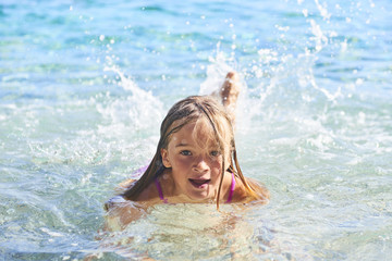 Child blond girl enjoying ocean waves on beach, summer vacation with children concept
