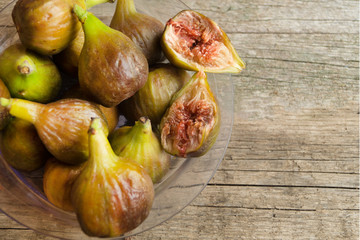 Ripe green and brown figs in the plastic plate on the wooden table