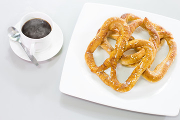 Pretzel bread white sesame in white dish and black coffee on gray background