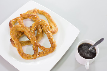 Pretzel bread white sesame in white dish and black coffee on gray background