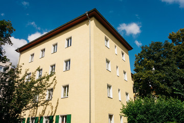 yellow apartment house inbetween of green trees and blue sky