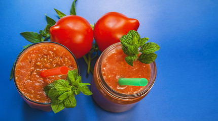Tomato smoothies with mint and straw. Red tomatoes. blue background. wide