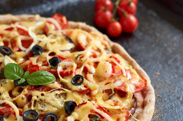 Hot vegetarian pizza with tomatoes, bell pepper, onion, black olives, cheese, spices on dark black baking tray background decorated with small cherry tomatoes close up with copy space. Side view
