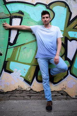 Young man posing beside a rustic wall painted with graffiti