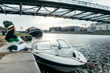 young pretty woman in hat sitting on pier in the morning