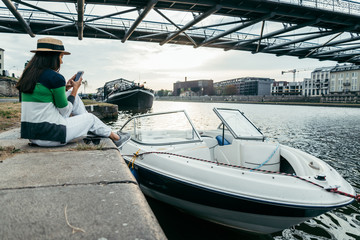 young pretty woman in hat sitting on pier in the morning