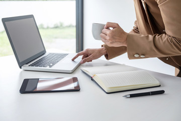 Young Entrepreneur woman manager working indoors at a modern office, typing and holding a coffee cup while using her laptop