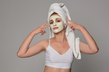 Beautiful female model with towel on her hear and white facial cosmetic mask on her face. Beauty cosmetic concept. Isolated on gray background.