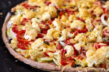 Fresh hot homemade veggie pizza with cutting vegetables - tomatoes, bell pepper, onion, cheese close up on a dark background. Side view