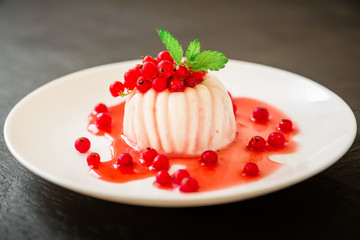 Sweet Jelly Panna Cotta with berries in white plate on a dark table. Tasty dessert.