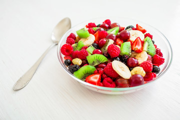 Tasty fruit salad in glass bowl with spoon on white table. Natural vegan food