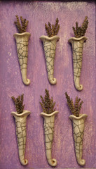 Pachnące,  suszone kwiaty lawendy powieszone na fioletowej ścianie w ceramicznych flakonikach.