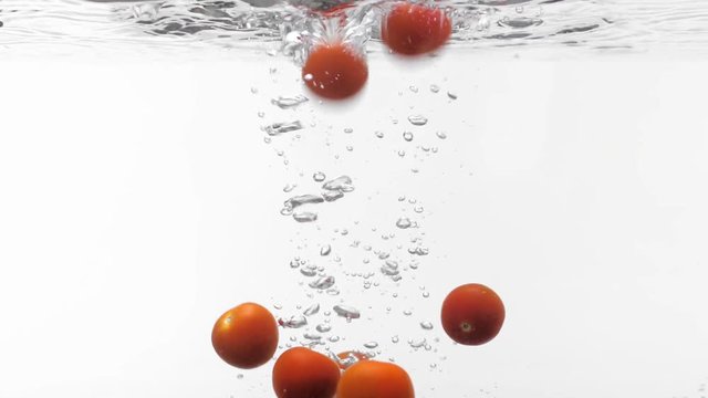 Slo-motion cherry tomatoes falling into water